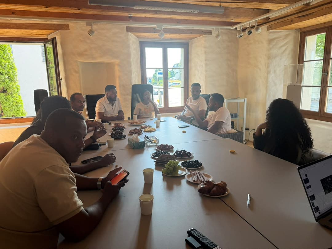 People seated around a long table, sharing snacks and conversation in a bright room with wooden beams